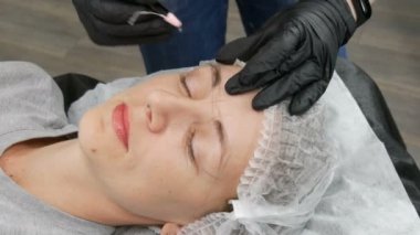 Kaş şekli düzeltme ustası kaşların yoğunluğunu vurgulamak için derinin altına özel koyu bir pigment uygular. Modern kozmetik prosedürleri, kaş mikro pateni, kalıcı makyaj, dövme.