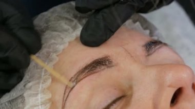 Kaş şekli düzeltme ustası kaşların yoğunluğunu vurgulamak için derinin altına özel koyu bir pigment uygular. Modern kozmetik prosedürleri, kaş mikro pateni, kalıcı makyaj, dövme.