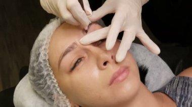 Usta özel kalemle kaşların yeni bir şeklini çizer. Kaş şekli düzeltmesi. Mikro patinaj, kalıcı makyaj, dövme