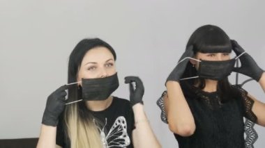 Kızlar aynanın önünde siyah tıbbi maskeler takarlar.