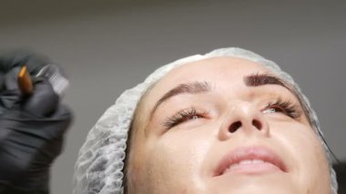 Mikro patinaj için özel bir kalem ve iğne yardımıyla kozmetolojist genç bir kadının kaşlarının şeklini geliştirir. Kaş mikropateni, kalıcı makyaj, dövme.