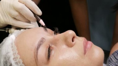 Usta özel kalemle kaşların yeni bir şeklini çizer. Kaş şekli düzeltmesi. Mikro patinaj, kalıcı makyaj, dövme