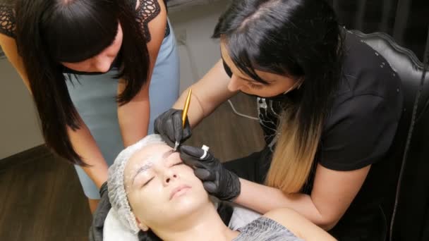 El maestro de micropatinaje enseña a su alumno a hacer la forma correcta de las cejas en el modelo. Maquillaje permanente, tatuaje, cambiar la nueva forma de las cejas — Vídeos de Stock