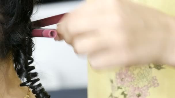 Μικρές μπούκλες στα μαύρα μαλλιά μιας νεαρής γυναίκας, κομμώτρια χρησιμοποιώντας ένα ειδικό καυτό σίδερο για μπούκλες — Αρχείο Βίντεο