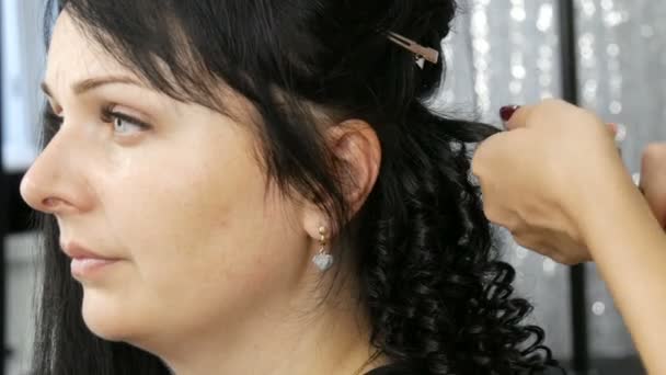 Kleine krullende krullen op het zwarte haar van een jonge vrouw, kapper met behulp van een speciale hete krultang — Stockvideo