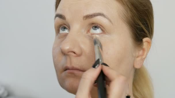 Professional evening make-up. Makeup artist applies foundation brush on the face and neck body of a young woman model. Cosmetic concept. — Stock Video