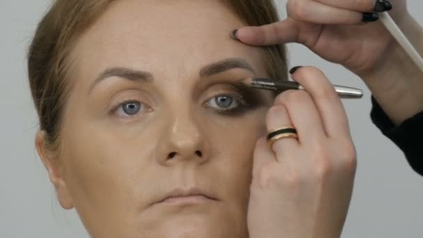 Professionell makeup artist gör beige makeup med en speciell penna för en ung kvinna modell med blå ögon. Kväll ljust rökig ögonmakeup — Stockvideo