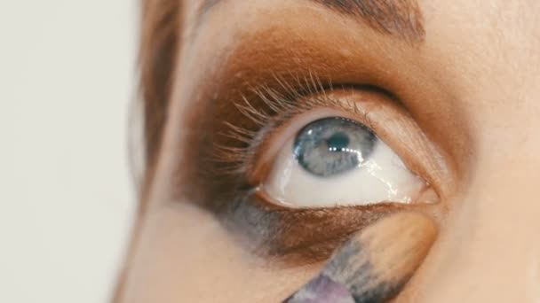 Professionell makeup artist gör beige makeup med en speciell borste för en ung kvinna modell med blå ögon närbild. — Stockvideo