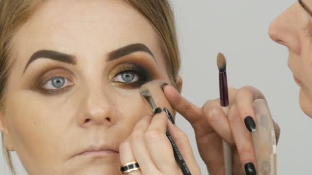 7 april 2019 - Kamenskoe, Ukraina: Master make-up artist tillämpa professionell make-up gyllene rökiga ögon i en skönhetssalong på en modell kvinna modell med blå ögon på nära håll — Stockvideo