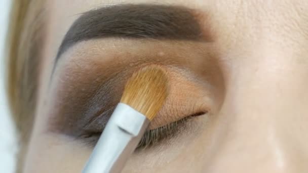 Master make-up καλλιτέχνης εφαρμογή επαγγελματική make-up χρυσά καπνιστά μάτια σε ένα σαλόνι ομορφιάς σε ένα μοντέλο γυναίκα μοντέλο με μπλε μάτια από κοντά — Αρχείο Βίντεο