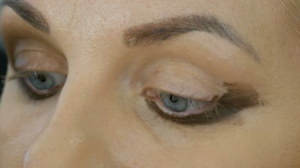 Professionell makeup artist gör beige makeup med en speciell penna för en ung kvinna modell med blå ögon. Kväll ljust rökig ögonmakeup — Stockvideo