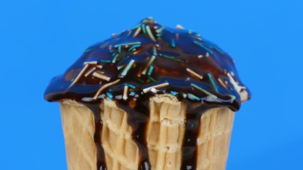 Шоколадний соус глазурування і барвисті зморшки тече над морозивом у вафельній чашці на синьому фоні — стокове відео