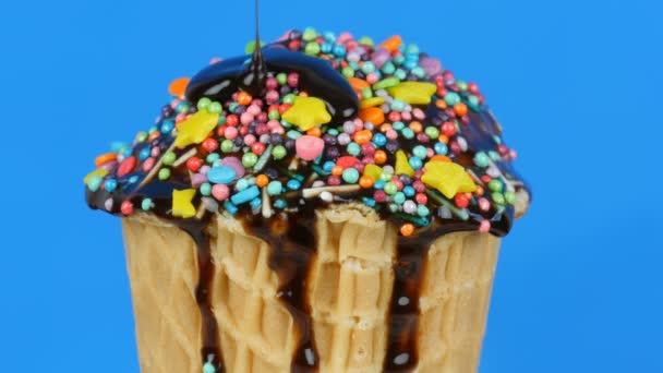초콜릿 소스와 화려 한 스프링 이 푸른 배경에 있는 와플 컵 위에 있는 아이스크림 위로 흐른다 — 비디오