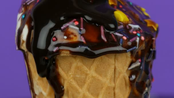 Ванильное мороженое украшено сверху красочными брызгами на светлом фиолетовом фоне. Шоколадный соус — стоковое видео