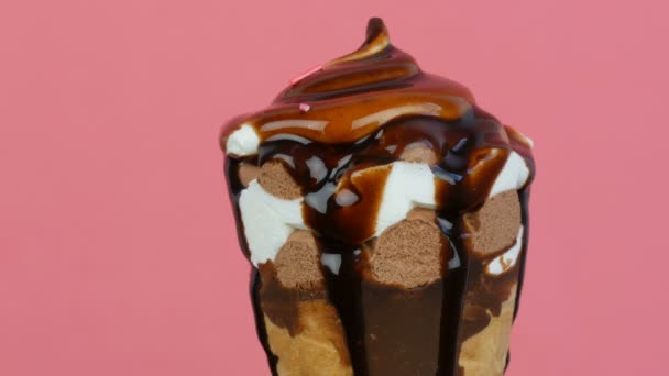 Chocolate sauce icing flows over ice cream in a waffle cup on pink background — Stock Video