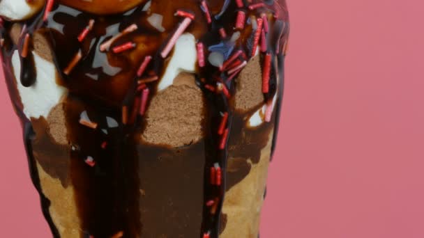 Chocolate sauce icing flow over ice cream in a waffle cup on pink background — Stok Video