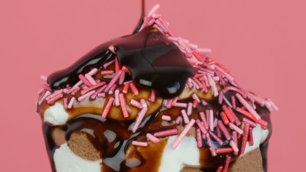Σάλτσα σοκολάτας άχνη ρέει πάνω από το παγωτό σε ένα Κύπελλο βάφλα σε ροζ φόντο — Αρχείο Βίντεο