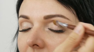 Özel fırça ile akşam kahverengi göz makyajı ve kaş yapıyor uzun siyah saçlı güzel bir mavi gözlü kadın modeli portresi