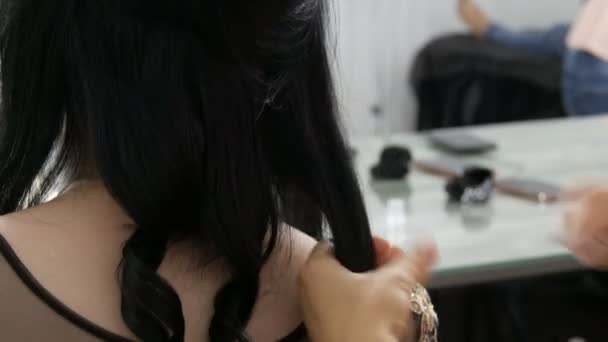 Профессиональная женщина парикмахерская расческа с длинными черными кудрями молодой красивой женщины, которая сидит сзади в праздничном вечернем платье — стоковое видео