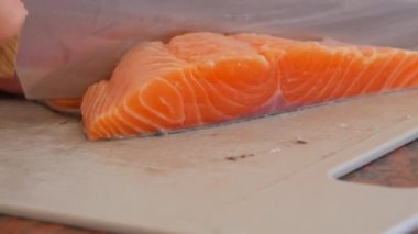 Erkek eller, ev mutfağındaki plastik bir tahtada büyük bir somon balığı filetosunu parçalara ayırıyor.