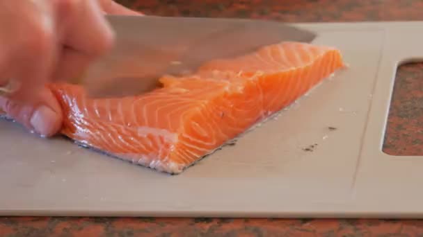 Мужские руки разрезали на куски огромное филе красной рыбы лосося на пластиковой доске на домашней кухне — стоковое видео