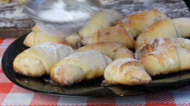 Üstünde pudra şekeri olan bereketli taze kruvasanlar. Ev yapımı hamur işleri, taze kruvasan çörekleri ev mutfağındaki özel bir süzgeçten pudra şekeri serpiştirilmiş.