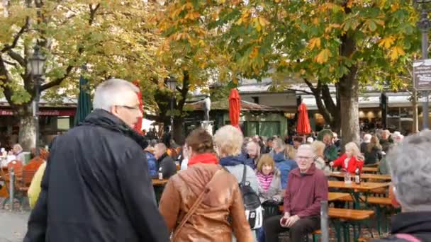 Munique, Alemanha - 24 de outubro de 2019: Pessoas não identificadas no famoso Viktualienmarkt. O famoso Biergarten de Munique no qual as pessoas relaxam. Turistas sentam-se à mesa no parque, bebem cerveja e comem — Vídeo de Stock
