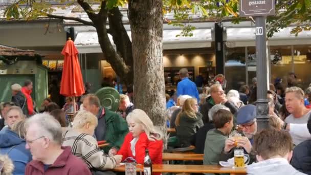 München, Németország - 2019. október 24.: Ismeretlen emberek a híres Viktualienmarktnál. A híres Müncheni Biergarten, ahol az emberek pihenhetnek. A turisták asztalhoz ülnek a parkban, söröznek és esznek. — Stock videók