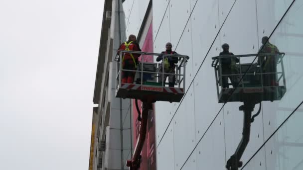 Munich, Allemagne - 25 octobre 2019 : Deux hommes nettoient le verre d'un centre d'affaires sur une grue spéciale. Un nettoyeur de verre pour homme qui travaille sur un ascenseur hydraulique lave les fenêtres dans un centre de bureaux de grande hauteur — Video