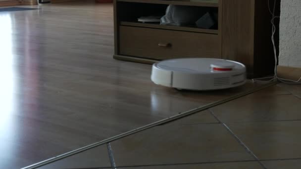 Un moderno aspirapolvere robot automatico bianco spazza i detriti sul pavimento in camera. Aspirapolvere bianco a rotazione con spazzole piccole, sensore touch motion. Pulizia autonoma della camera. Assistente domestico intelligente — Video Stock