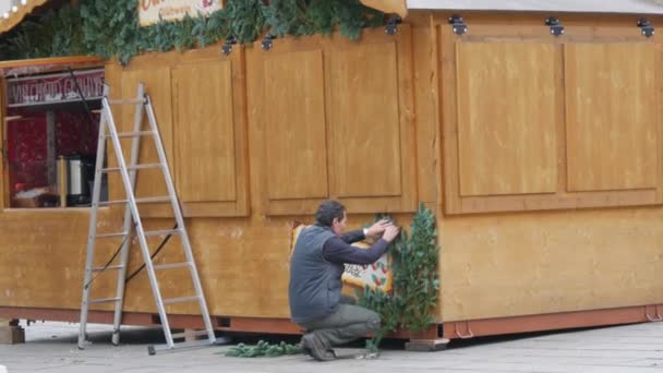 STRASBOURG, FRANCIE - NOV 22, 2021: Příprava na vánoční trhy. Muž zdobí dřevěný kiosek jedlovými větvemi — Stock video