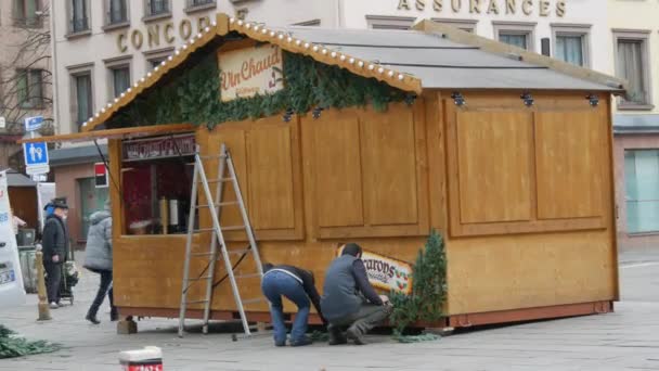 STRASBOURG, FRANCIA - 22 NOV 2021: Preparazione per i mercatini di Natale. Un uomo decora un chiosco di legno con rami di abete — Video Stock
