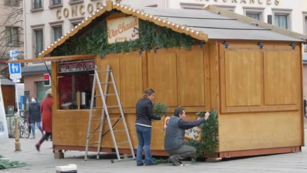 STRASBOURG, FRANCIE - NOV 22, 2021: Příprava na vánoční trhy. Muž zdobí dřevěný kiosek jedlovými větvemi — Stock video