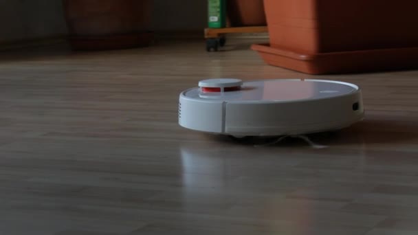 Een moderne witte automatische robot Stofzuiger veegt puin op de vloer in de kamer. Een rotatie witte stofzuiger met kleine borstels, aanraking bewegingssensor. Autonome schoonmaak van de ruimte. Slimme thuisassistent — Stockvideo