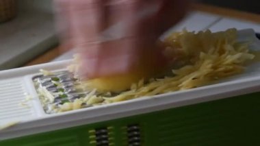 Erkek elleri vejetaryen yemek pişirmek için mutfak rendesine patates sürüyor.