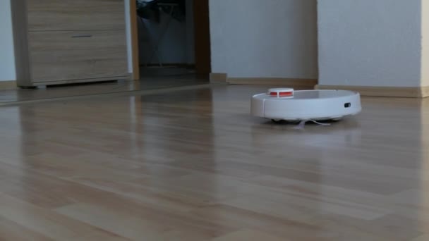 Een moderne witte automatische robot Stofzuiger veegt puin op de vloer in de kamer. Een rotatie witte stofzuiger met kleine borstels, aanraking bewegingssensor. Autonome schoonmaak van de ruimte. Slimme thuisassistent — Stockvideo