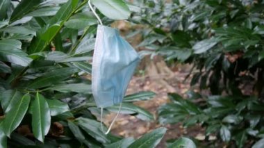 Terk edilmiş bir tıbbi maske sokak çalılığında asılı duruyor. Covid Coronavirus 19 ile savaşmanın sonuçları. İnsan kirliliği kavramı