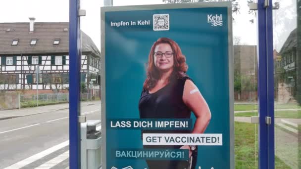 11 december 2021 - Kehl, Tyskland: En affisch som uppmanar till vaccinet Covid19 vid en busshållplats, med inskription på tyska, engelska och ryska. Förebyggande av bekämpning av influensavirus — Stockvideo