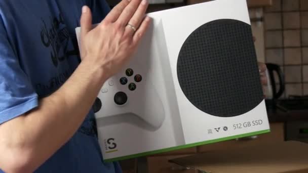 9 Desember 2021 Kehl, Jerman: Seorang pria dengan senang hati membelai sebuah kotak dengan Xbox di dalam rumah. Konsol permainan video rumah yang dikembangkan oleh Microsoft. — Stok Video