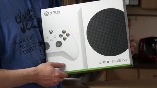 9 december 2021 - Kehl, Tyskland: En man stryker glatt en låda med en Xbox i huset. Hem TV-spel konsol utvecklad av Microsoft. — Stockvideo