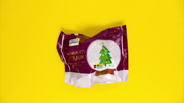 Kehl, Alemania - 4 de diciembre de 2021: Una barra de chocolate y una caja de Navidad en forma de árbol aparecen repentinamente sobre un fondo amarillo. Chocolates dulces para niños. Detener animación en movimiento — Vídeos de Stock