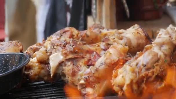 Egy nagy, zsíros, szaftos disznóöklöt grillsütőn sütnek a tűz hátterében. Utcai ételfesztivál, szabadtéri piknik — Stock videók