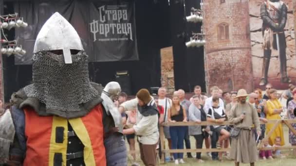 Trostyanets, Ukraine - August 21, 2021: Spectators look with interest at reproduction of medieval battle. People dressed in knightly armor and metal helmets and shields fight with cold steel — Stock Video