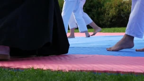 Las piernas de los atletas en kimono que se dedican a la lucha libre callejera en karemats especiales. Entrenamiento masivo de atletas de karate — Vídeos de Stock