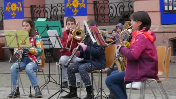 Генгенбах, Германия - 15 декабря 2021 года: Детский оркестр играет на разных музыкальных инструментах на улице, перед зданием, слушает главного учителя — стоковое видео