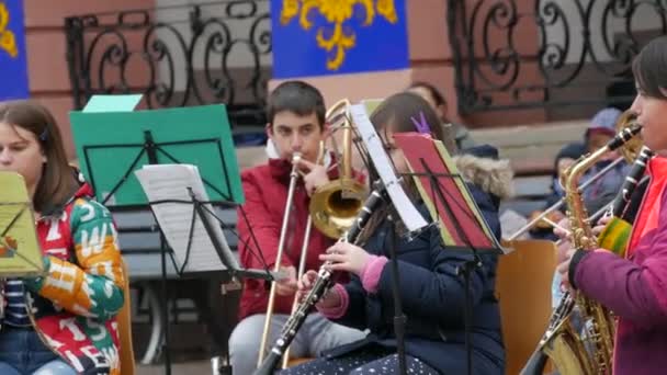 德国根根巴赫- 2021年12月15日：儿童管弦乐队在街上的建筑物前演奏不同的乐器，聆听主要老师的演奏 — 图库视频影像