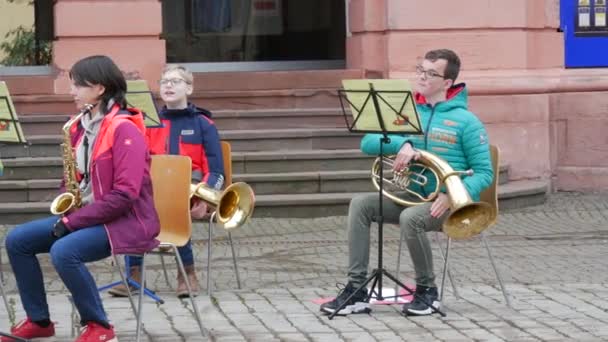 德国根根巴赫- 2021年12月15日：儿童管弦乐队在街上的建筑物前演奏不同的乐器，聆听主要老师的演奏 — 图库视频影像
