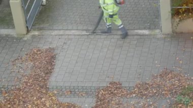 Açık yeşil takım elbiseli hademeler, özel rüzgar üfleyicilerinin yardımıyla düşen kuru yaprakları temizliyorlar.