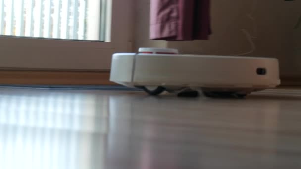 Современный белый автоматический пылесос-робот выбрасывает мусор на пол в комнате. Поворотный белый пылесос с маленькими щетками, сенсор движения касания. Автономная уборка комнаты. Умный домашний помощник — стоковое видео