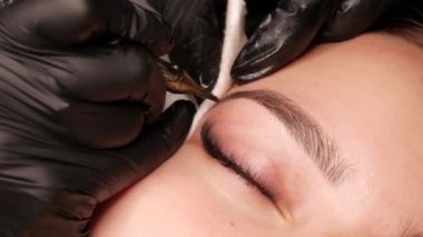 Kaş kalıcı makyaj malzemesi. Stüdyodaki usta, özel bir makine kullanarak genç bir modelin derisinin altında siyah pigmenti tanıtıyor. Güzellik için modern dövme